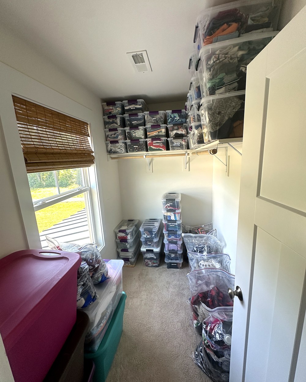 The same closet after organizing, with matching labeled bins neatly arranged on shelves and a clear floor