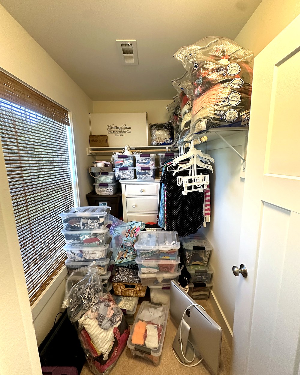 Cluttered walk-in closet before organizing, with storage bins and bags stacked on the floor