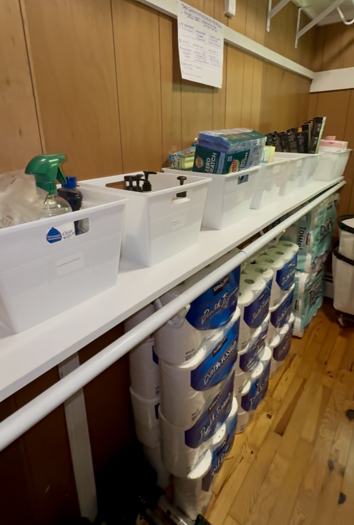 Cleaning headquarters shelving with labeled bins of supplies and a full restock of paper towels and toilet paper