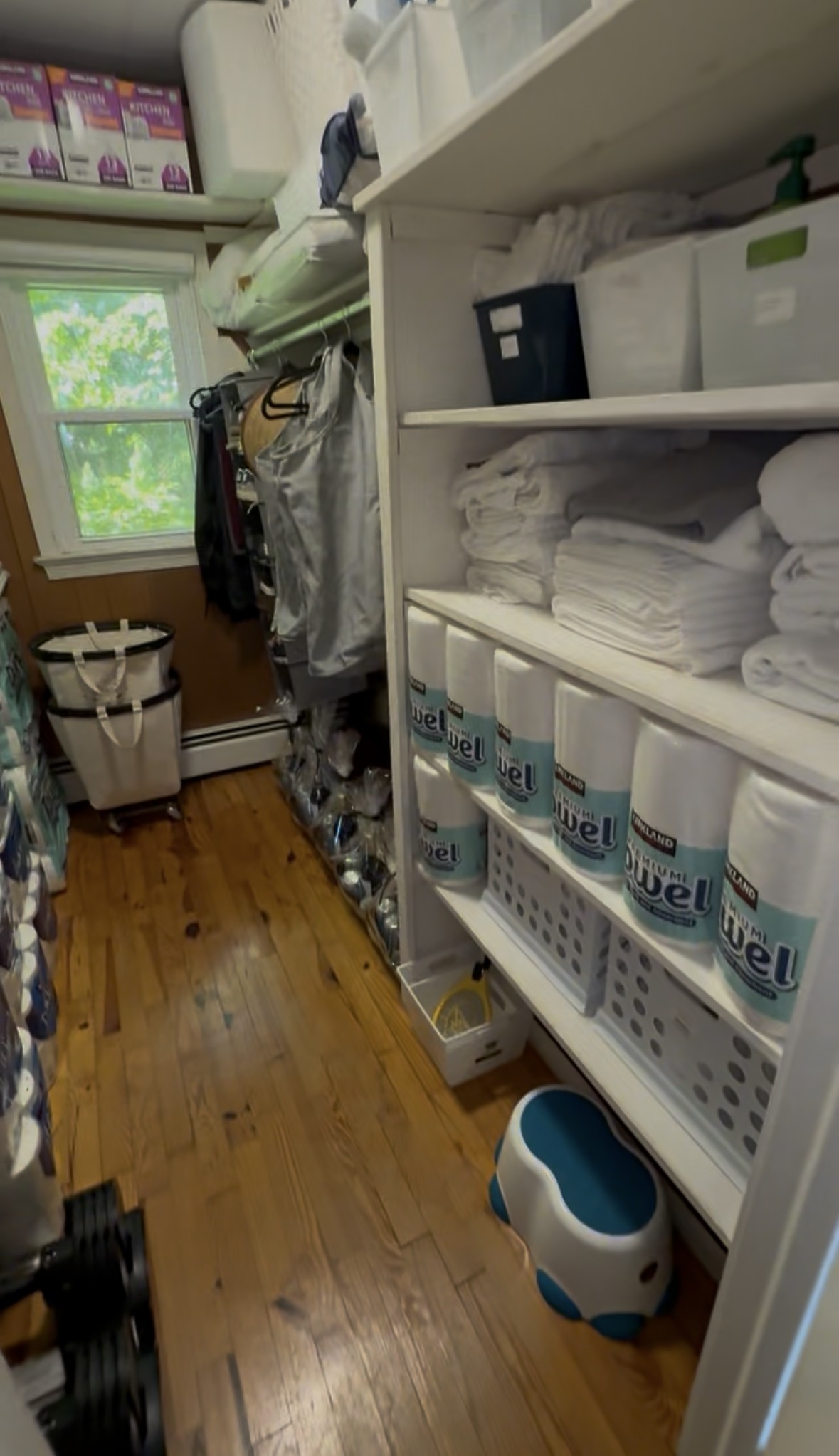 Linen closet shelving with folded towels and a full restock of paper products, organized and labeled